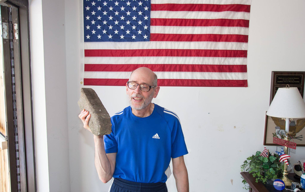 A man holds up the brick that was throown throught the glass door.